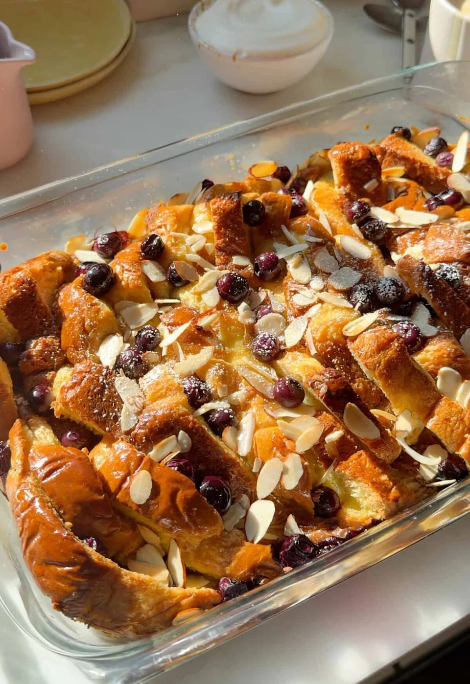 Baked bread pudding topped with sliced almonds and blueberries in a glass dish