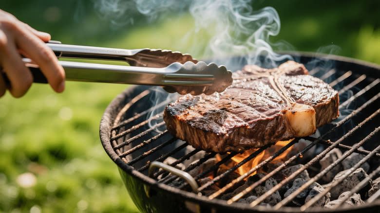 A person cooking a t-bone steak on a grill