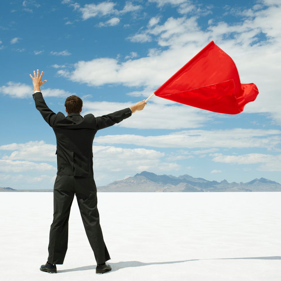 Person in a suit waving a red flag outdoors.