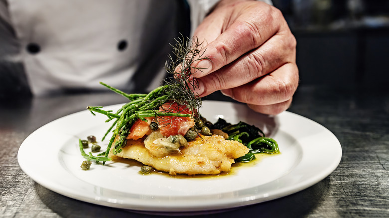 A chef adding garnish to a fish dish