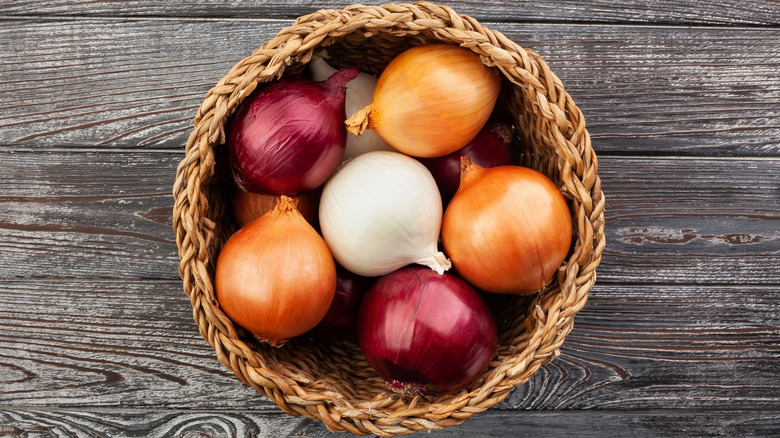 Red, white, and orange onions in a basket, against a rustic background