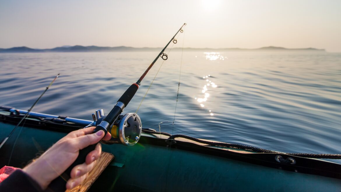 Experts recommend harvesting, cooking invasive lionfish to curb their spread in US waters A person holding a fishing rod over calm water with sun reflections and distant hills.