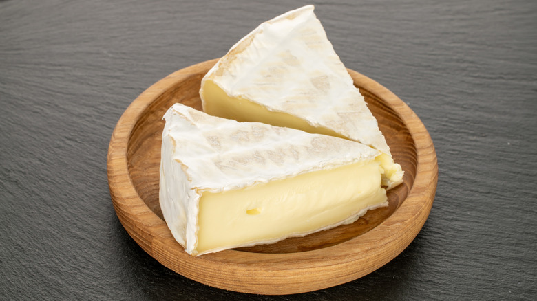 Two slices of brie cheese in wooden dish on table.