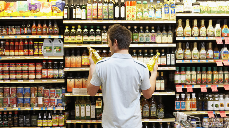 A grocery store shopper comparing different types of oil.