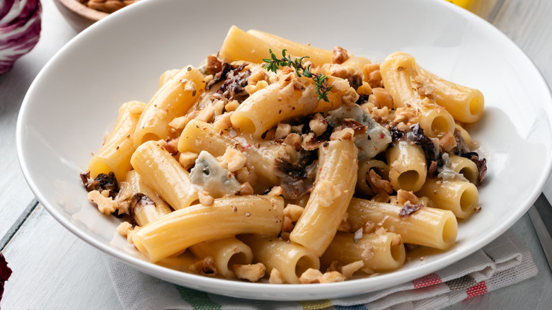 Thick tube shaped pasta noodles with creamy sauce, walnuts, and vegetables in white bowl