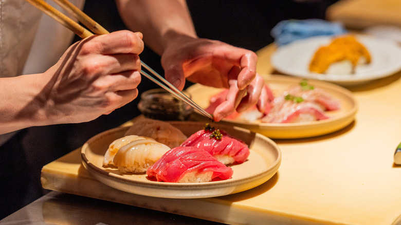 Sushi being arranged on a wooden plate by hands holding chopsticks