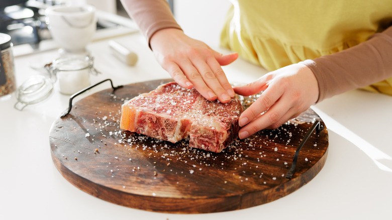 A person seasoning a t-bone steak