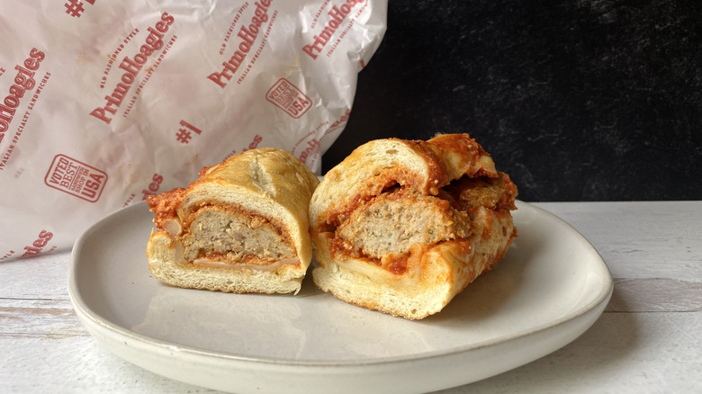 A Primo's meatball sub cut in half on a small plate in front of the to-go packaging
