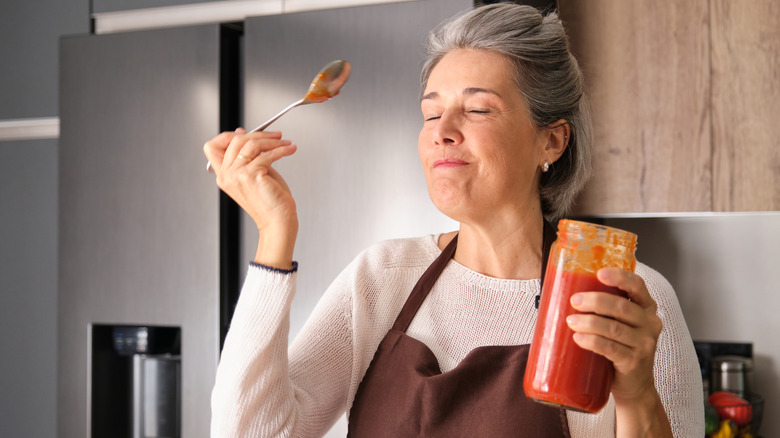 Woman tasting jar of marinara sauce