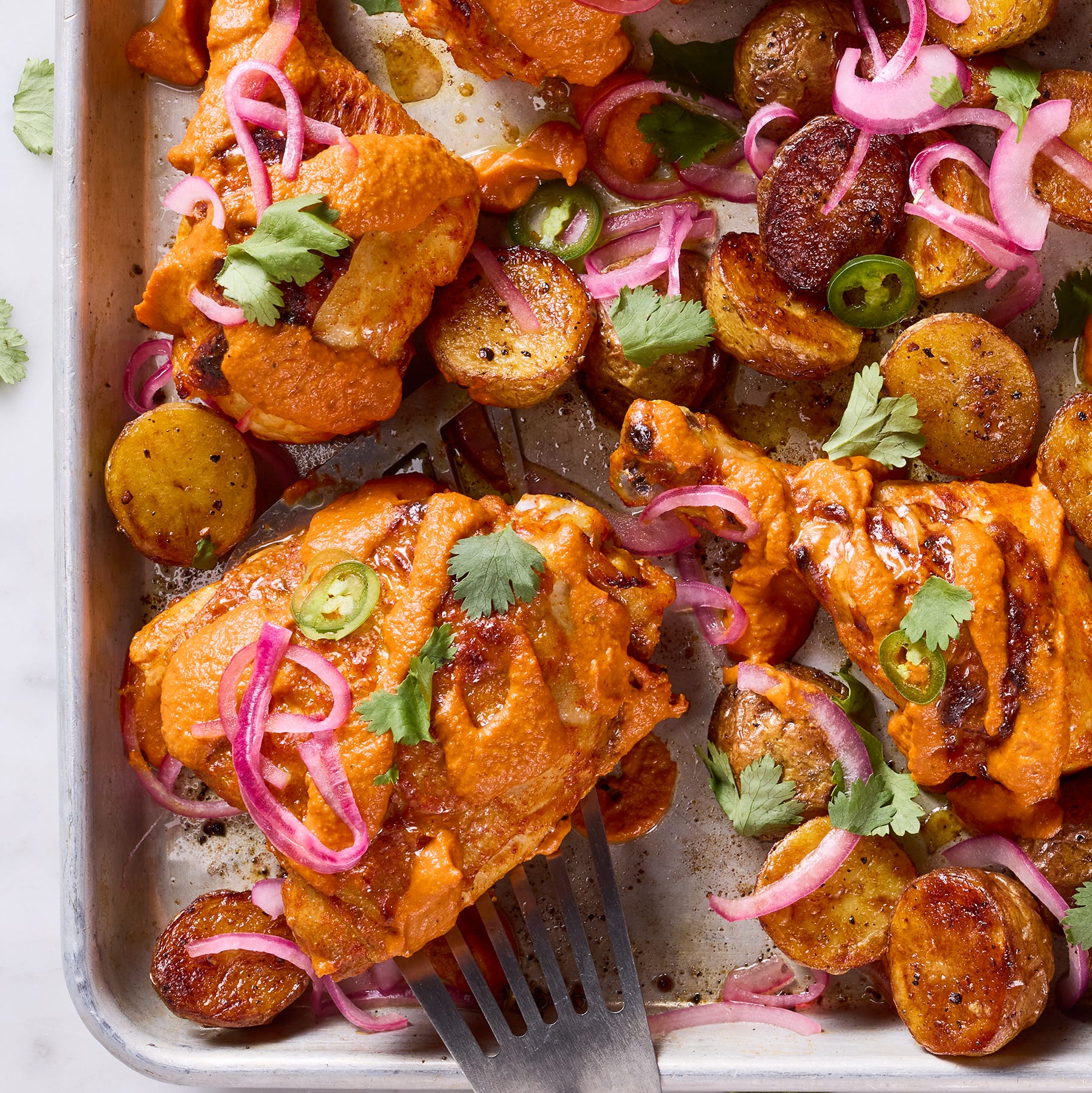 chicken thighs covered in a tikka masala sauce with pickled red onions and jalapenos on a sheet pan
