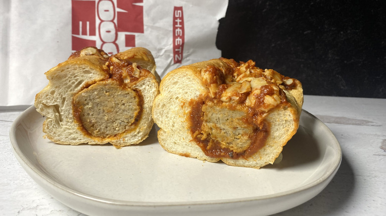 A Sheetz meatball sub sliced in half on a plate in front of the to-go packaging