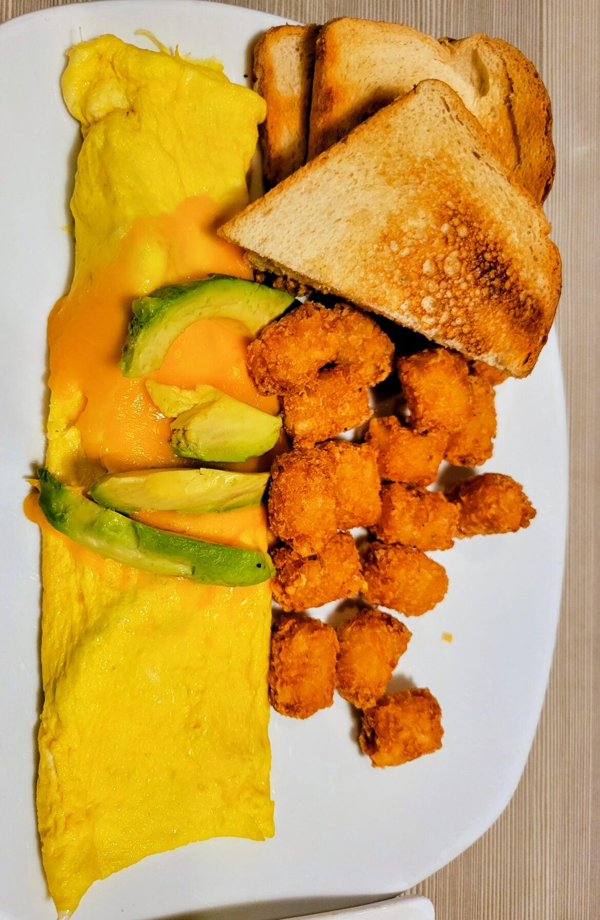 A cheddar and avocado omelet served with white toast and tater tots.