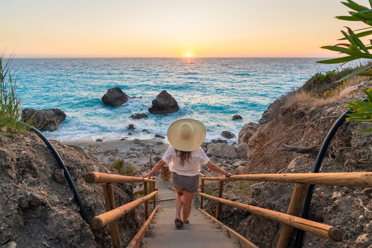 Woman with straw hat descending the steps to Kavalikefta Beach at sunset, Lefkada