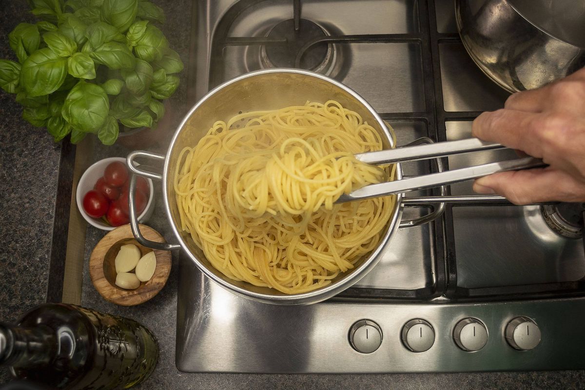 Kitchen tongs serving cooked spaghetti from a saucepan.