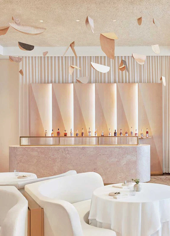 Modern, minimalist bar interior with sculptural ceiling elements, elegant seating, and bottles displayed on a stone counter.