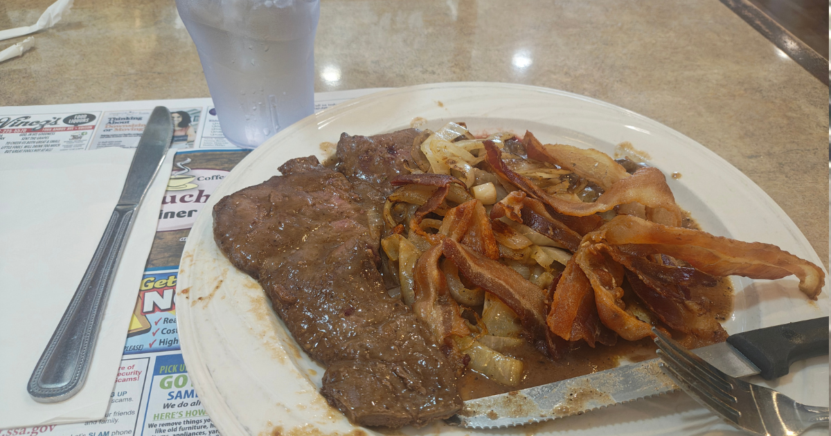 A large platter of liver and onions, with a tangle of bacon strips on top. 
