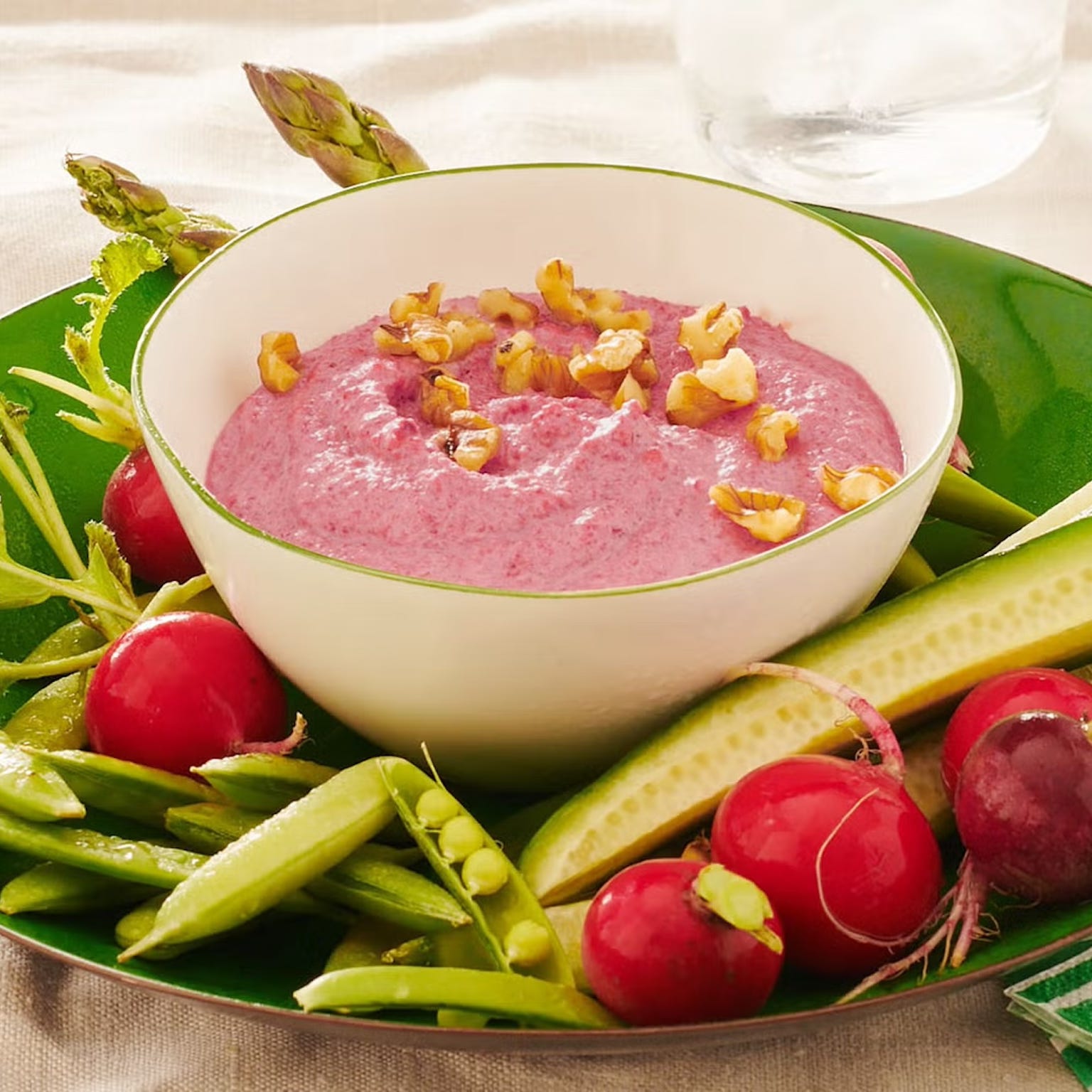 A bowl of pink dip surrounded by fresh vegetables.