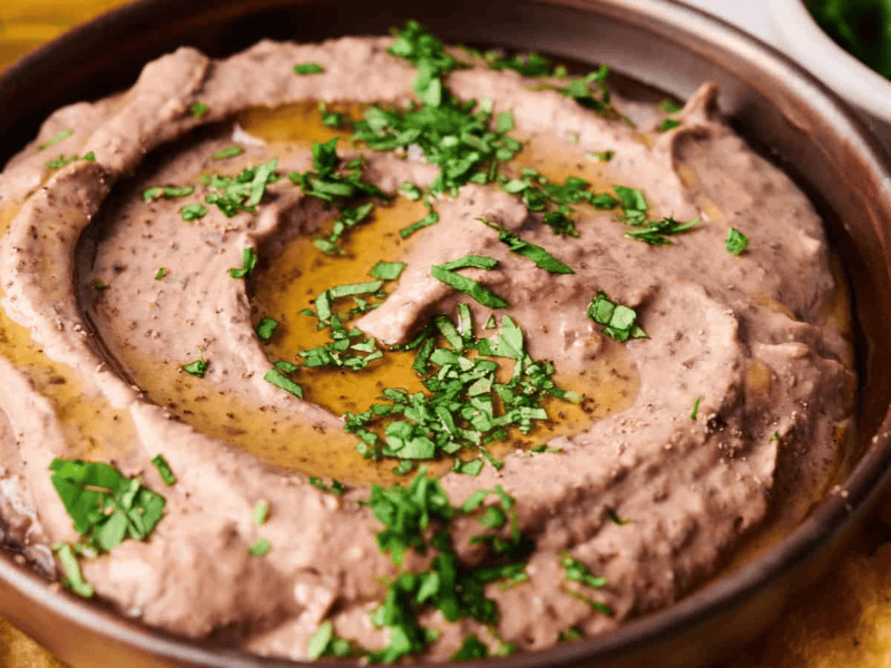 A bowl of bean dip garnished with chopped herbs and olive oil, surrounded by tortilla chips.