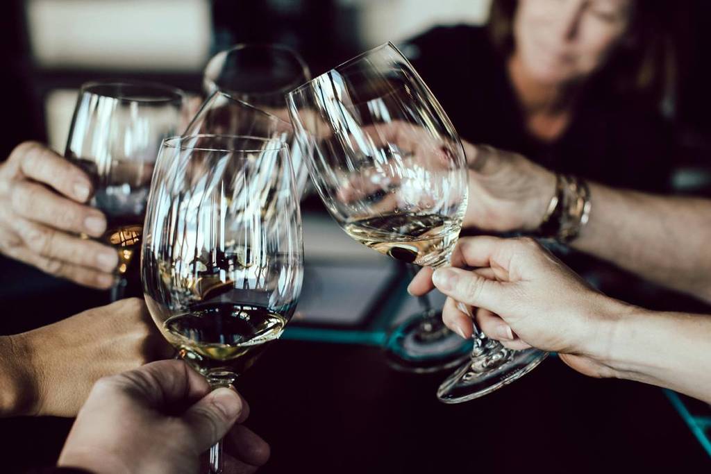 Close up of a group of people clicking white wine glasses