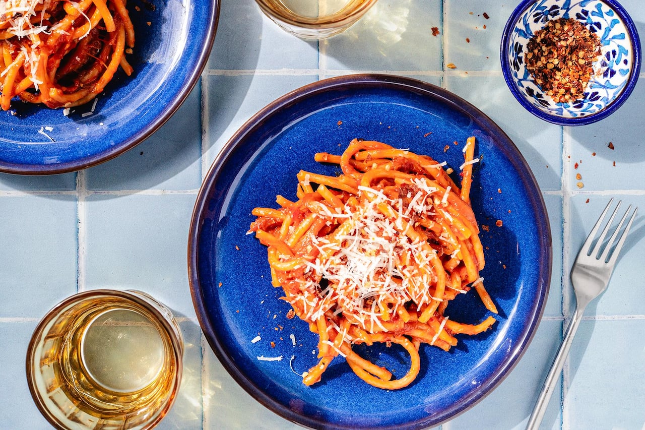 Top down shot of a blue plate of bucatini with tomato sauce topped with parmesan. 