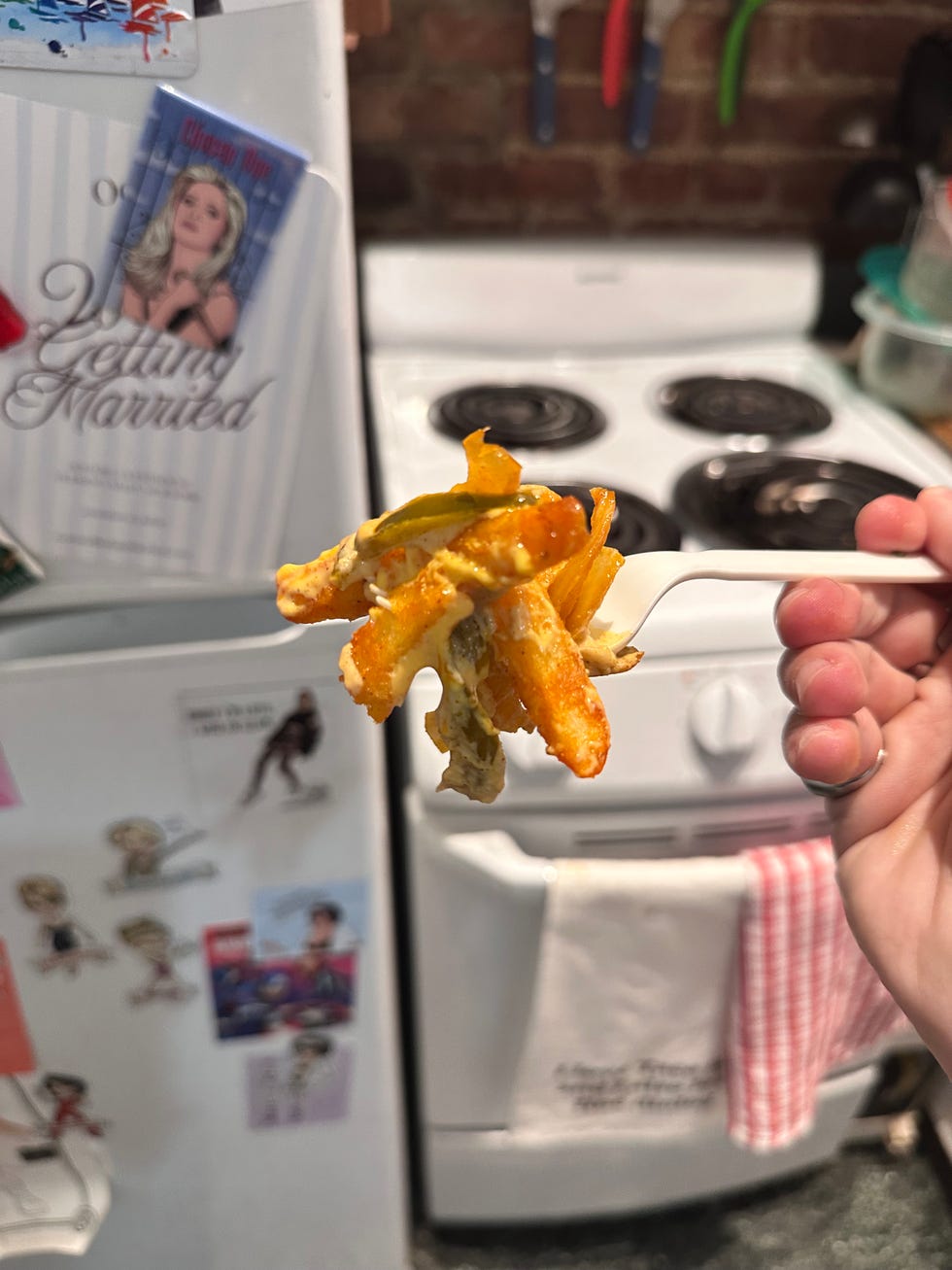Person holding a fork with cheesy fries in a kitchen. Person holding a fork with cheesy fries in a kitchen.