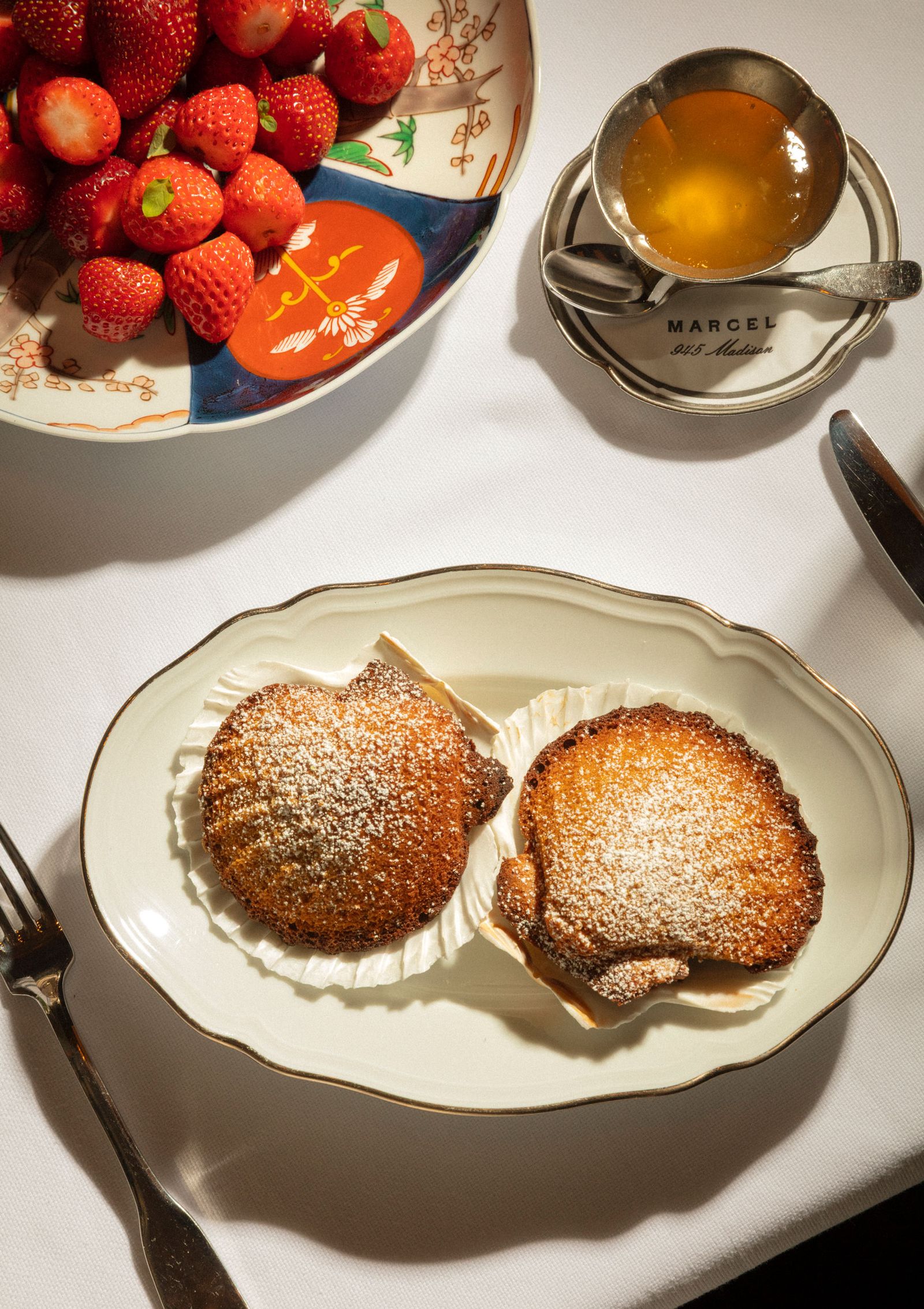 Two madeleines in seashells with strawberries and jam.