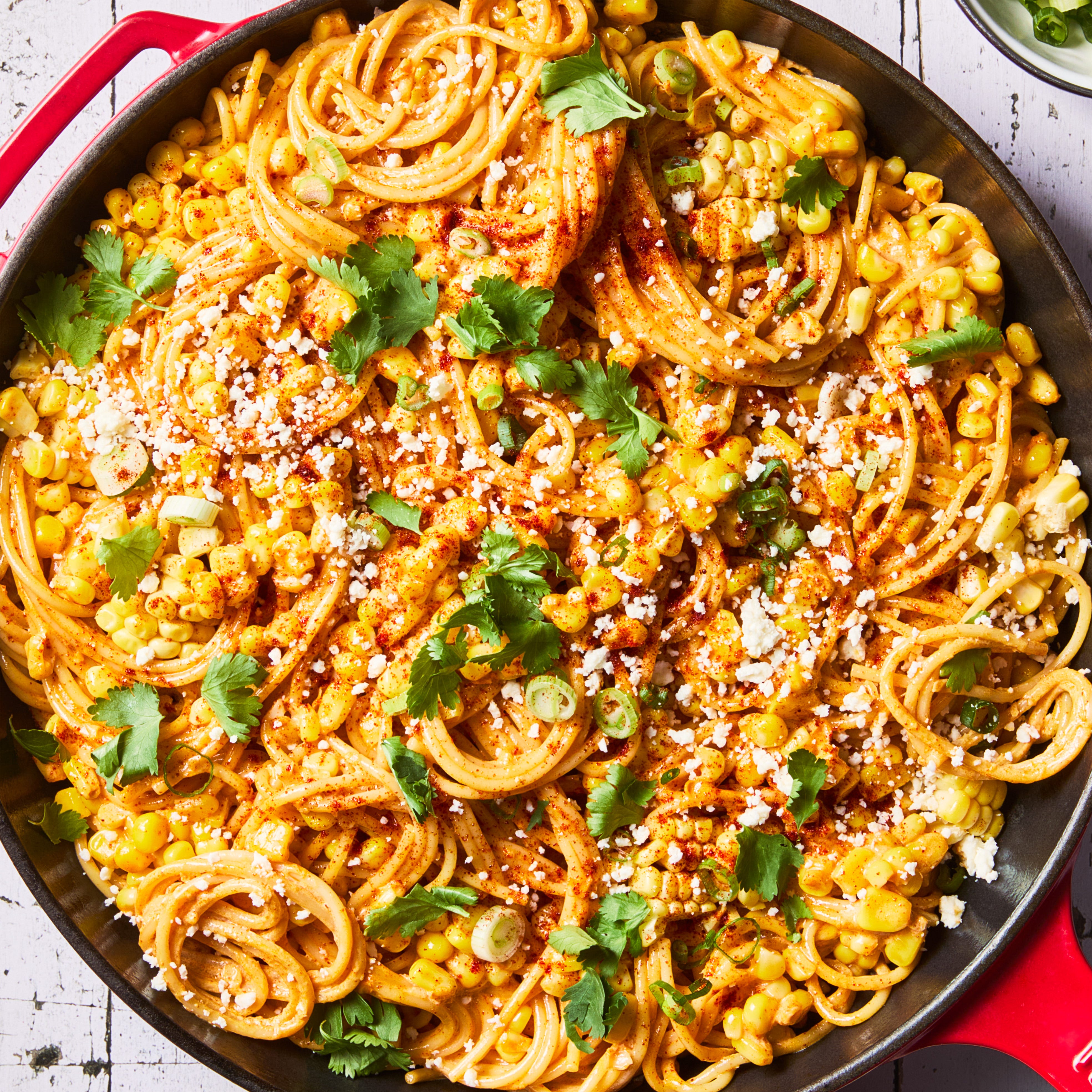 Spaghetti with corn, cheese, cilantro, and spices in a skillet.
