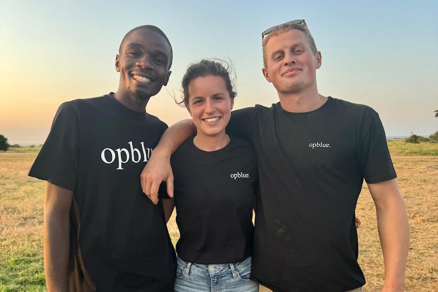 Three people smile with their hands around each other.