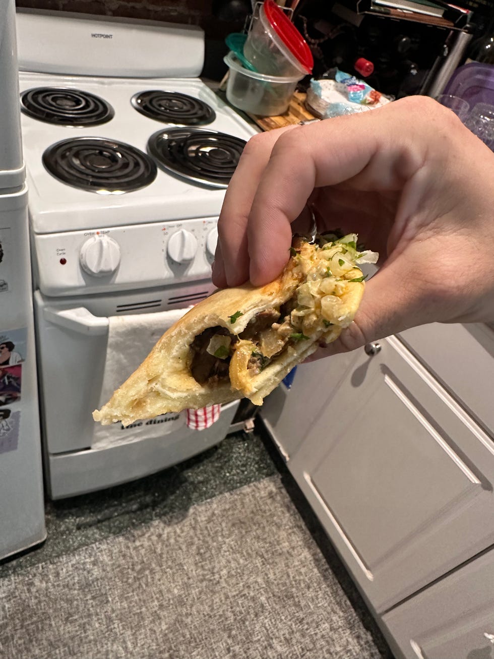 Hand holding a stuffed pita in a kitchen setting. Hand holding a stuffed pita in a kitchen setting.