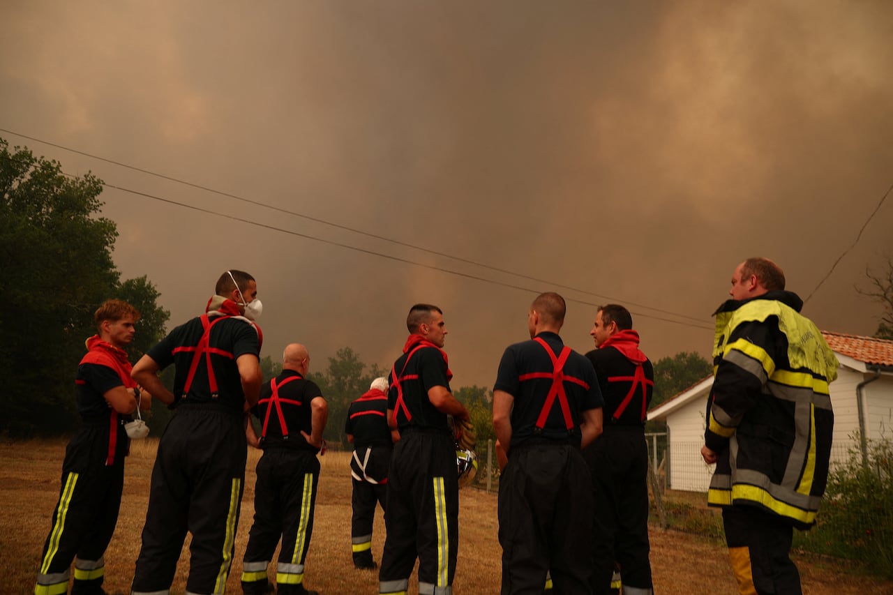 Firefighters stand as a wildfire burns nearby.