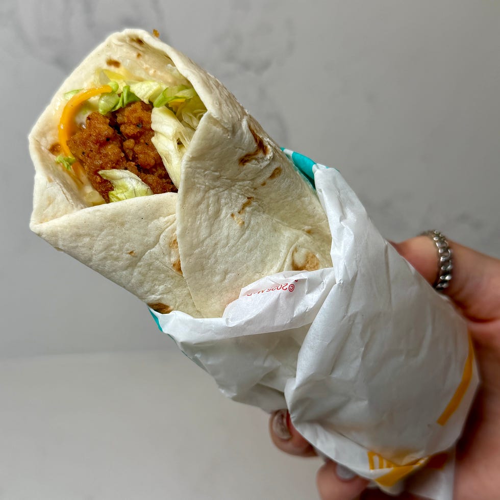 A hand holding a wrapped tortilla filled with lettuce, cheese, and meat. A hand holding a wrapped tortilla filled with lettuce, cheese, and meat.