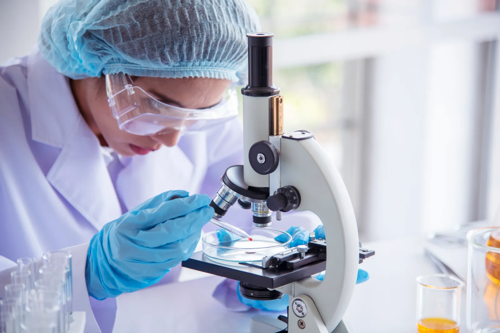A stock image shows a scientist in lab looking at a microscope during a medical test.