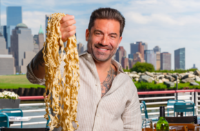 Chef Ryan DePersio holds up a fistful of pasta outside his restaurant Battello in Jersey City, NJ, with the Manhattan skyline behind him