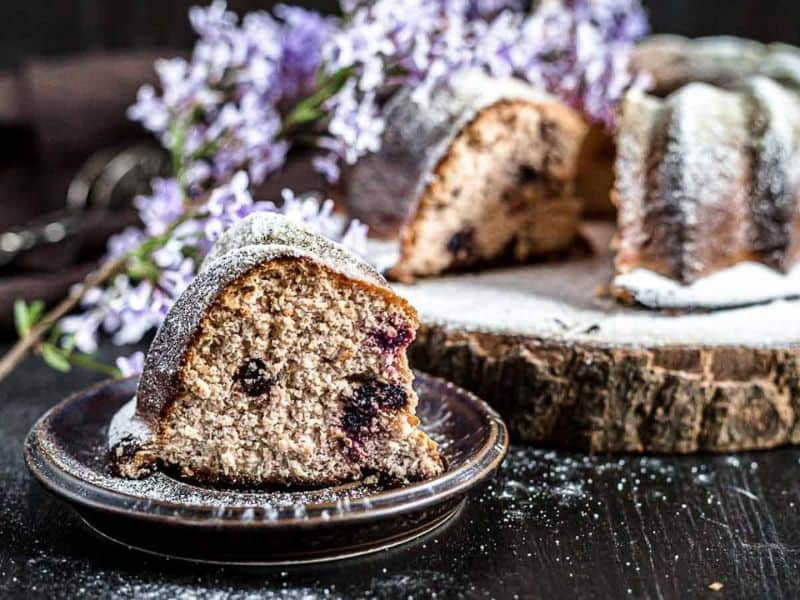 Farmers Cheesecake Keto Bundt Cake on a plate with flowers behind.