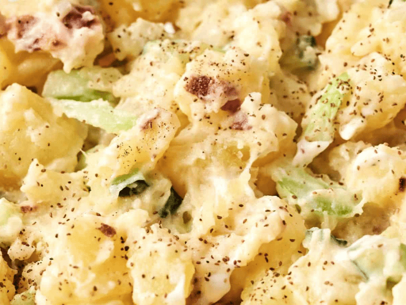 Close-up of creamy potato salad with chopped celery and black pepper seasoning.