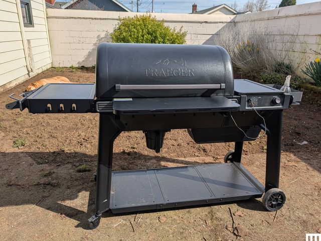 Front view of Traeger Woodridge Pro pellet smoker resting in a grass-free backyard with a white fence in the background