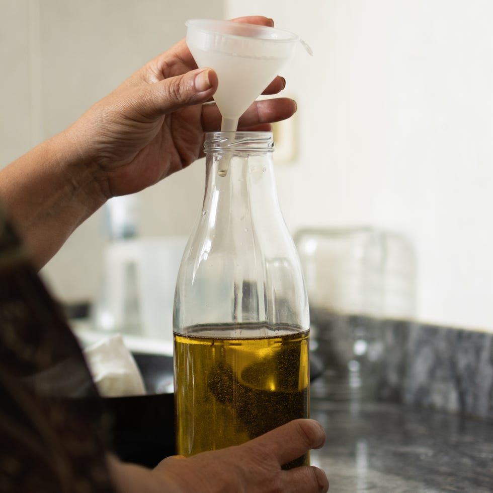 woman in the kitchen at home filling a glass bottle with used olive oil for cooking.recycling concept,zero waste in the water and sustainability and environment.vertical image
