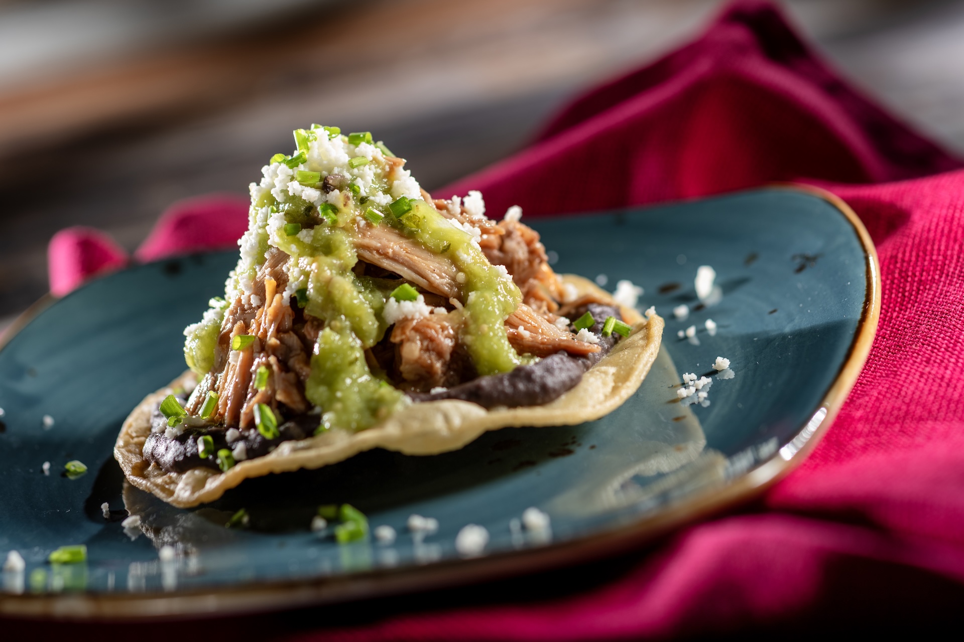 Tostada de Osso Buco: Pork osso buco atop a fried corn tortilla with chipotle black beans, salsa verde, queso fresco, and chives (New)