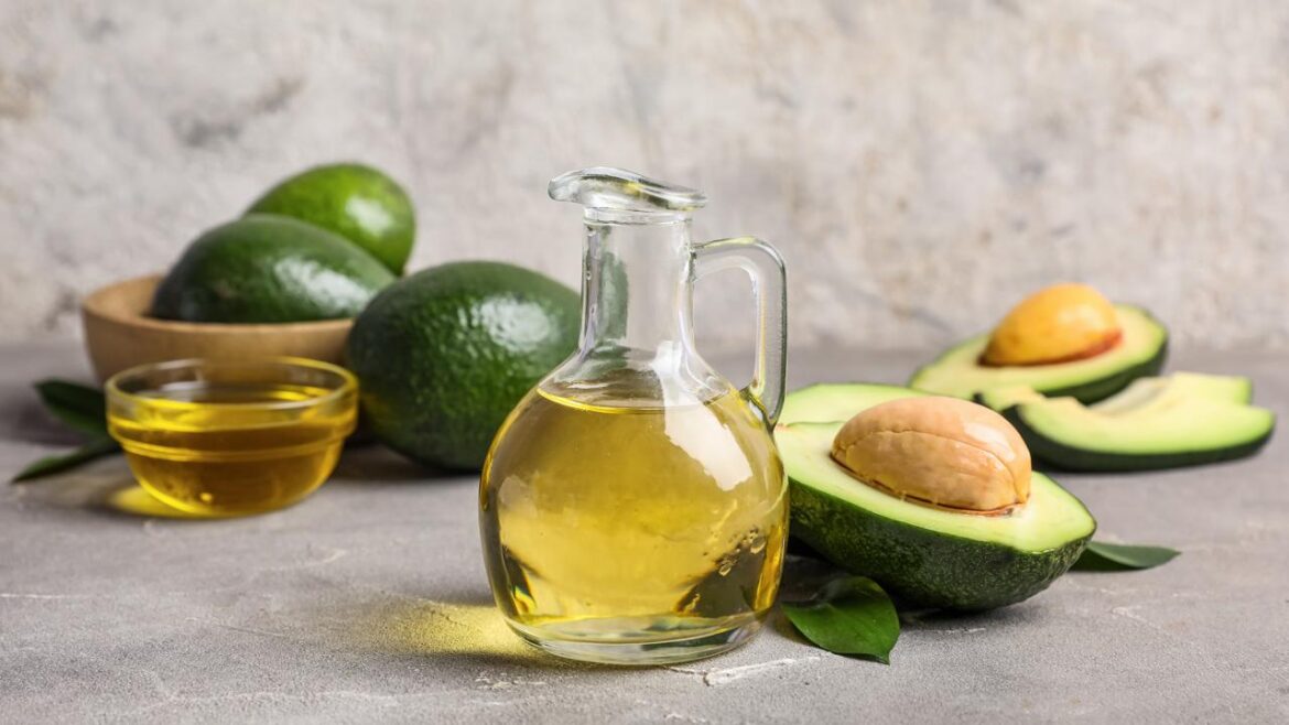 Food Fraud in Plain Sight Glass bottle and bowl of golden avocado oil with whole and halved avocados on gray surface