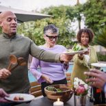 Man serving friends salad at backyard dinner party - stock photo