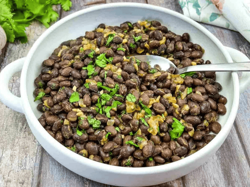 Mexican black beans in a white bowl with parsley and garlic.