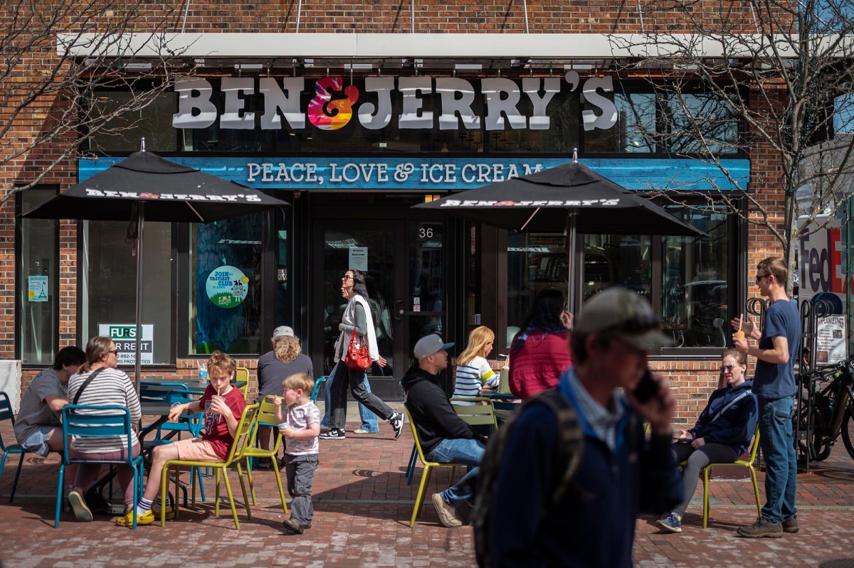 People sitting outside a Ben & Jerry's ice cream shop on a sunny day, with pedestrians walking past.