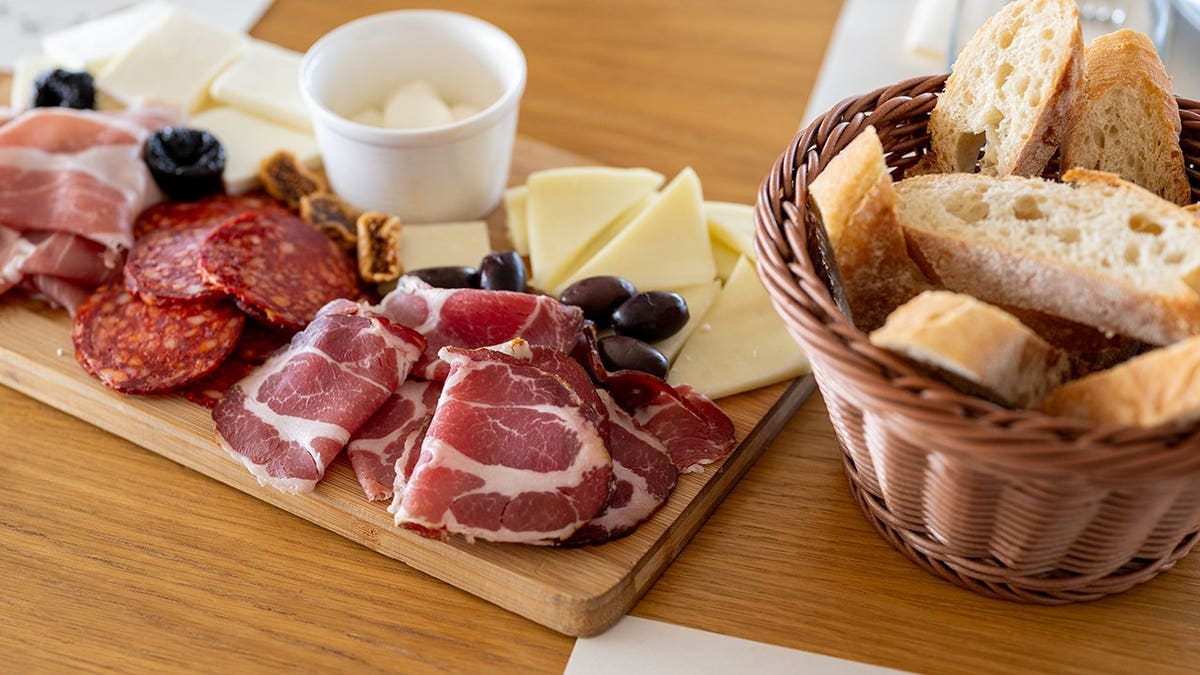 Charcuterie board with assorted cheeses, cured meats, chorizo, mozzarella, olives, figs and prunes on wooden board.