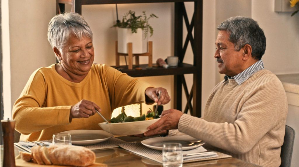  happy senior couple sitting down to enjoy a healthy meal together at home
