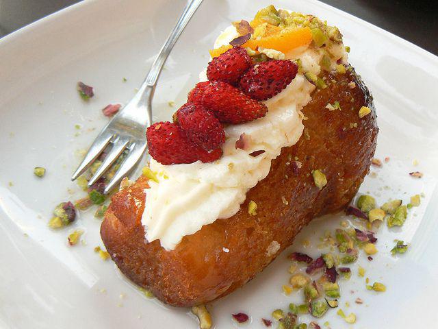 Baba: story of one of the symbols of Neapolitan cuisine baba in a plate with wild strawberries and pistachio flakes