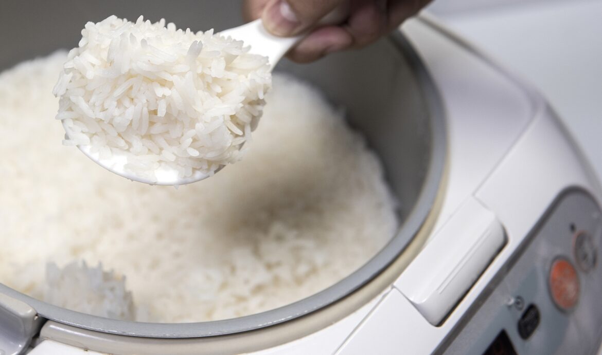 A spoonful of cooked rice is being lifted from a rice cooker.
