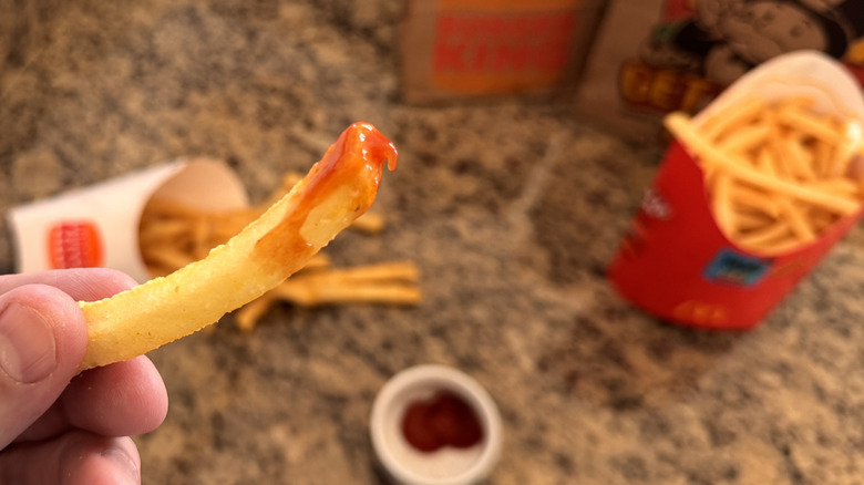 hand holding Burger King fry dipped in ketchup
