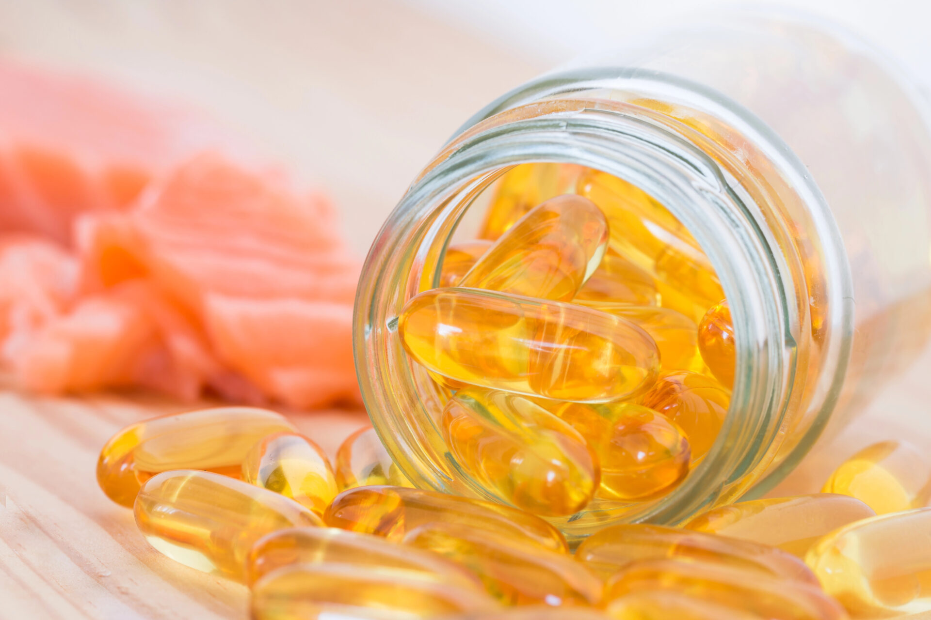 Pure omega salmon oil capsul in the bottle and piles on wooden table with backdrop is salmon.